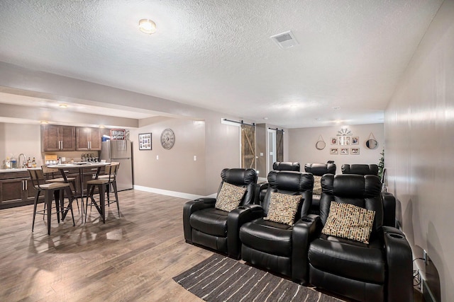 18481 N Fruitport Rd, Spring Lake, MI 49456 - cinema with a barn door, light wood-style flooring, a textured ceiling, baseboards, and bar