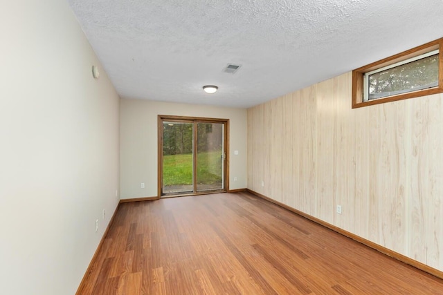 unfurnished room featuring a textured ceiling, light hardwood / wood-style flooring, and wood walls