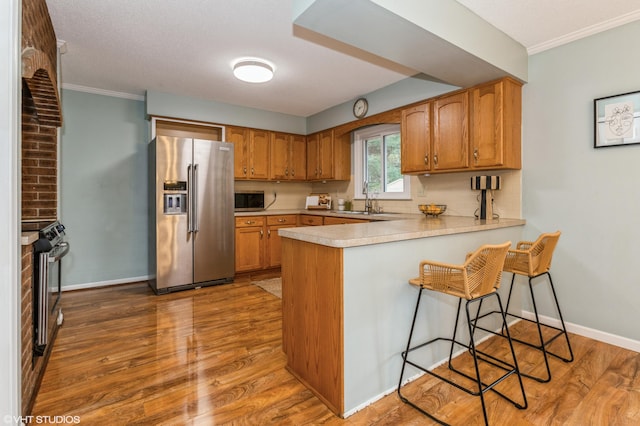 kitchen with a kitchen bar, kitchen peninsula, stainless steel appliances, sink, and light hardwood / wood-style flooring