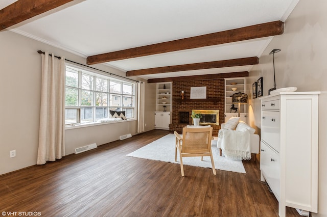 living room with beamed ceiling, dark hardwood / wood-style floors, built in shelves, and a brick fireplace