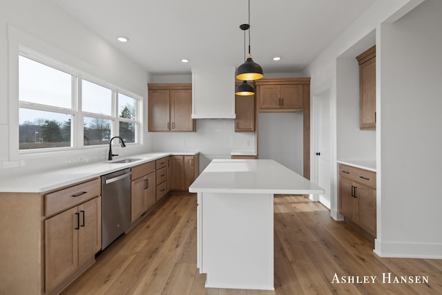 kitchen with pendant lighting, sink, light hardwood / wood-style flooring, stainless steel dishwasher, and a kitchen island