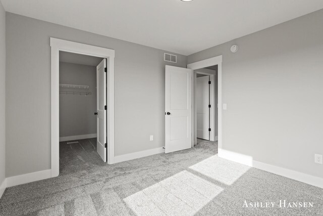 unfurnished bedroom featuring a walk in closet, a closet, and light colored carpet