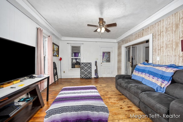 living room featuring hardwood / wood-style floors, ceiling fan, wood walls, and ornamental molding