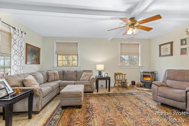 living room featuring beam ceiling, a wood stove, a wealth of natural light, and light hardwood / wood-style flooring