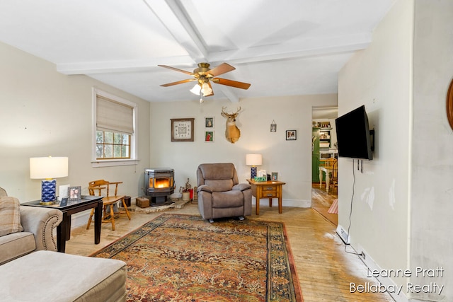 living room with beamed ceiling, ceiling fan, light wood-type flooring, and a wood stove