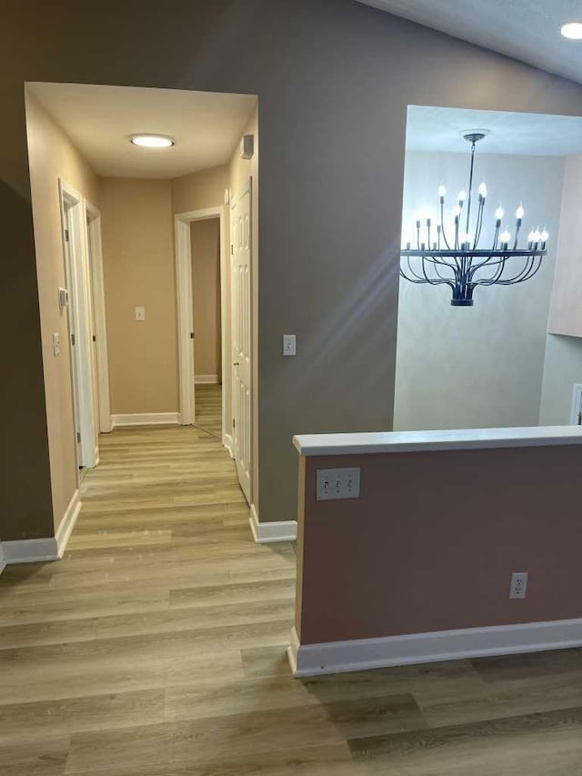 corridor with light hardwood / wood-style floors, an inviting chandelier, and lofted ceiling