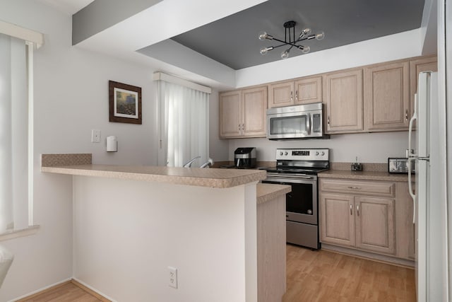 kitchen with a notable chandelier, light hardwood / wood-style floors, kitchen peninsula, and appliances with stainless steel finishes