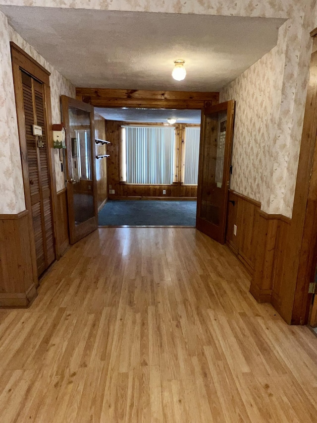 unfurnished room featuring light hardwood / wood-style floors, wood walls, a textured ceiling, and beam ceiling