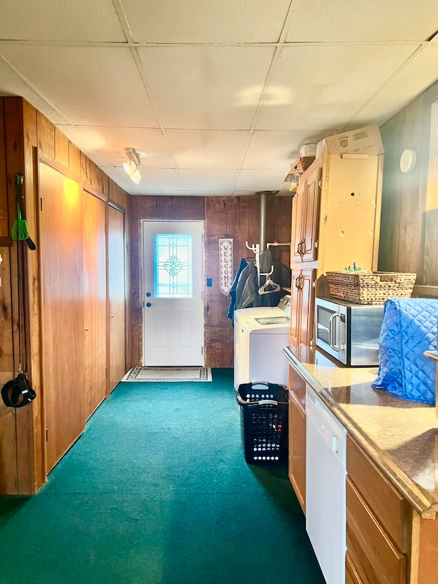 misc room featuring dark colored carpet, a drop ceiling, wood walls, and washer / clothes dryer