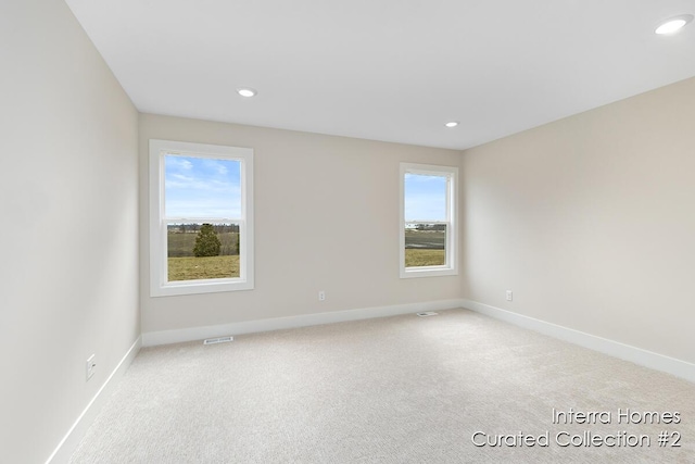 spare room with baseboards, plenty of natural light, and light colored carpet