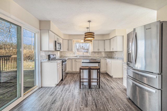 kitchen with a kitchen bar, appliances with stainless steel finishes, dark hardwood / wood-style flooring, pendant lighting, and a kitchen island