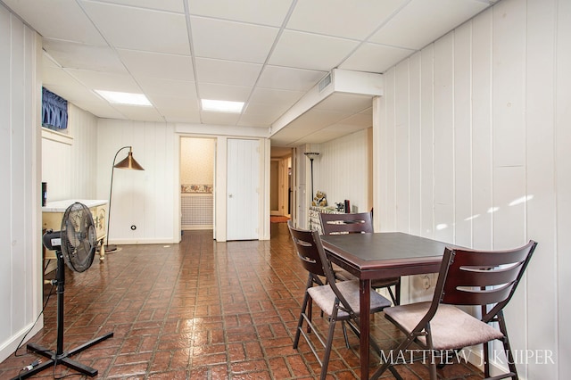 dining space featuring wood walls and a drop ceiling