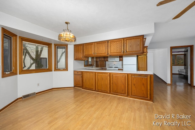 kitchen with kitchen peninsula, light wood-type flooring, white appliances, and decorative light fixtures