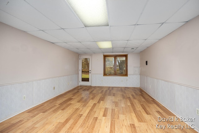 unfurnished room featuring a drop ceiling, light wood-type flooring, and wooden walls