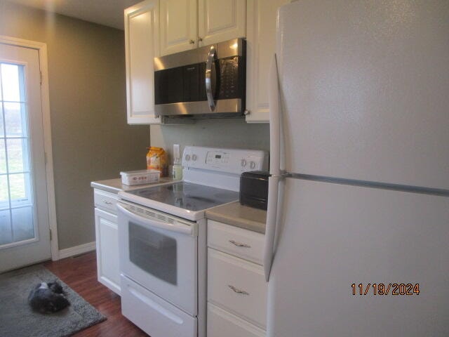 kitchen with white cabinets, dark hardwood / wood-style flooring, and white appliances