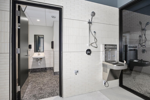 bathroom with tile patterned flooring, tiled shower, sink, and tile walls