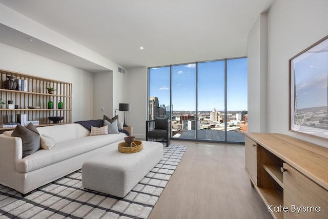 living room featuring a wall of windows, light wood-type flooring, visible vents, and a view of city