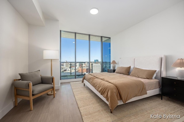 bedroom with expansive windows, wood finished floors, access to exterior, and baseboards