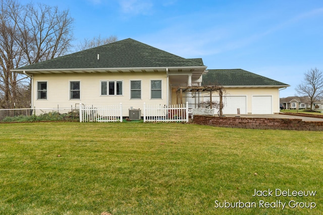 back of property with a garage, cooling unit, and a lawn