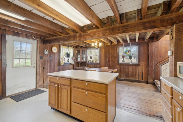 kitchen featuring wooden walls, beam ceiling, decorative light fixtures, a kitchen island, and a chandelier