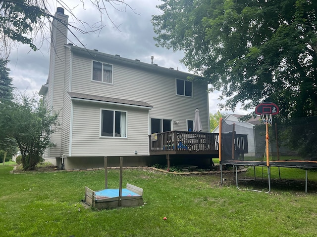 rear view of house featuring a trampoline, a deck, and a lawn