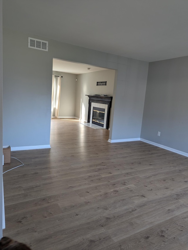 unfurnished living room featuring wood-type flooring and a tiled fireplace