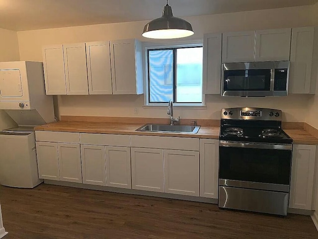 kitchen with stacked washing maching and dryer, stainless steel appliances, sink, white cabinetry, and hanging light fixtures