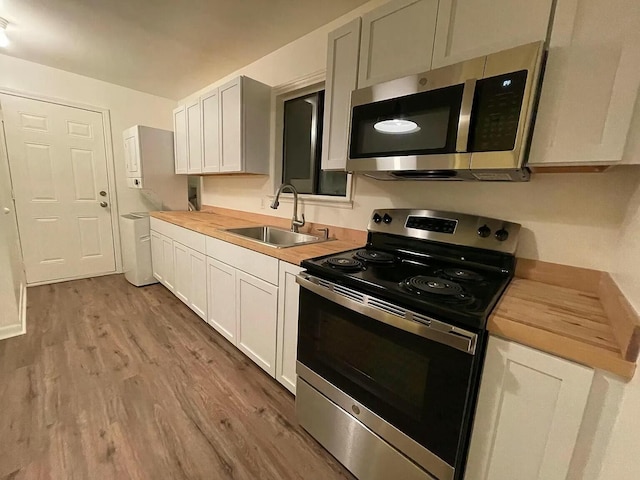 kitchen with hardwood / wood-style floors, white cabinets, sink, butcher block counters, and stainless steel appliances