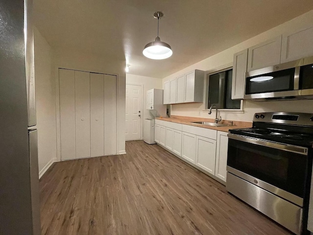 kitchen with stainless steel appliances, sink, pendant lighting, light hardwood / wood-style floors, and white cabinetry