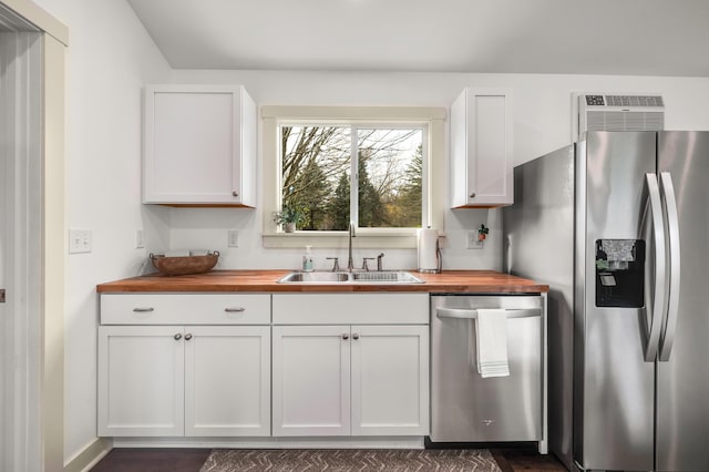 kitchen with appliances with stainless steel finishes, butcher block countertops, white cabinetry, and sink