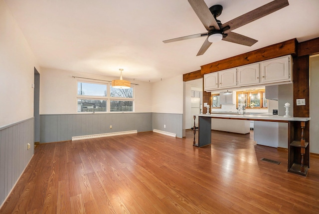 unfurnished living room with ceiling fan, a baseboard heating unit, and light hardwood / wood-style flooring