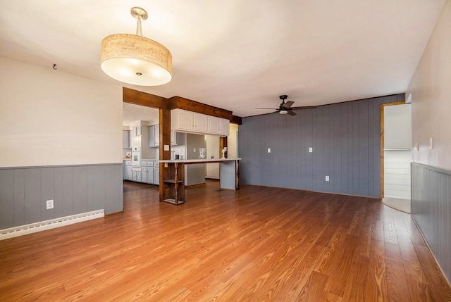 unfurnished living room featuring baseboard heating, ceiling fan, wood-type flooring, and wood walls