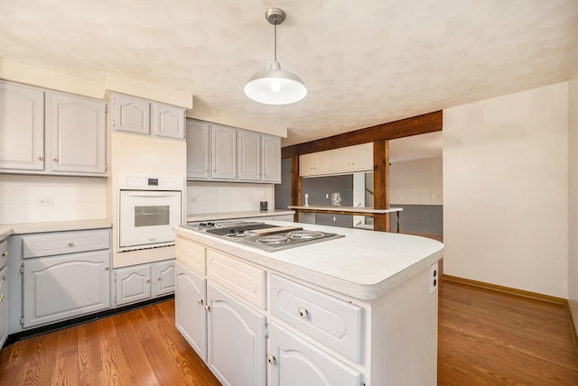 kitchen with stainless steel gas cooktop, pendant lighting, a center island, light hardwood / wood-style floors, and oven