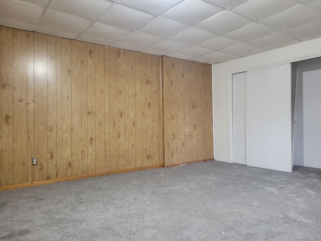 basement with carpet floors, a drop ceiling, and wooden walls