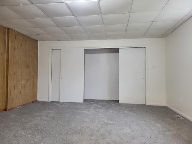 interior space featuring a drop ceiling, carpet floors, wooden walls, and a closet