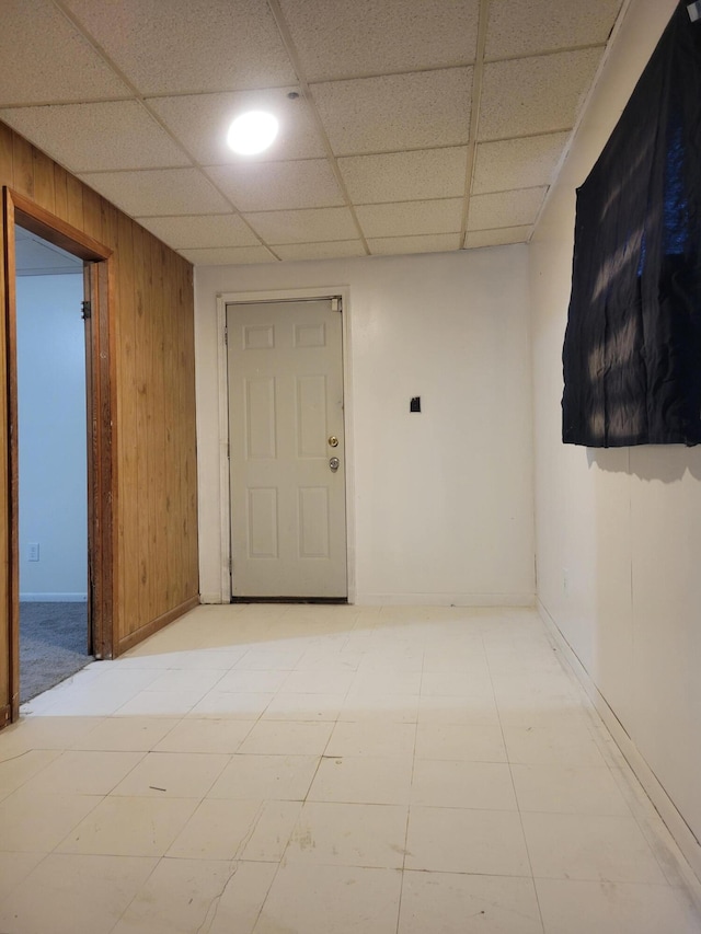 unfurnished room featuring a paneled ceiling and wooden walls