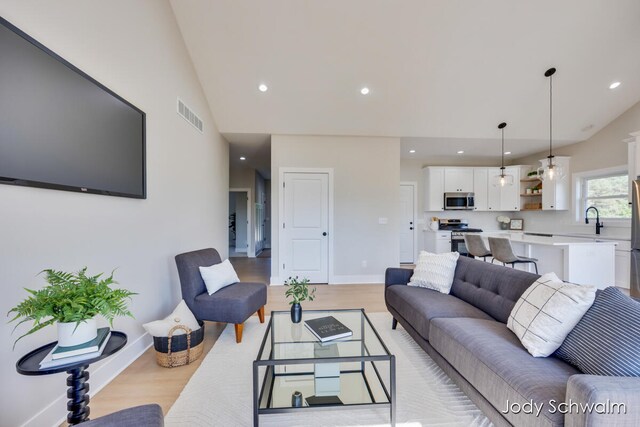 living room with light hardwood / wood-style floors, lofted ceiling, and sink