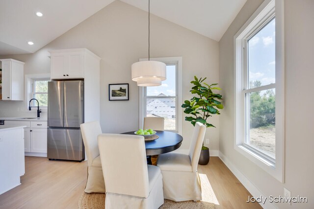 dining room featuring plenty of natural light, light hardwood / wood-style floors, sink, and high vaulted ceiling