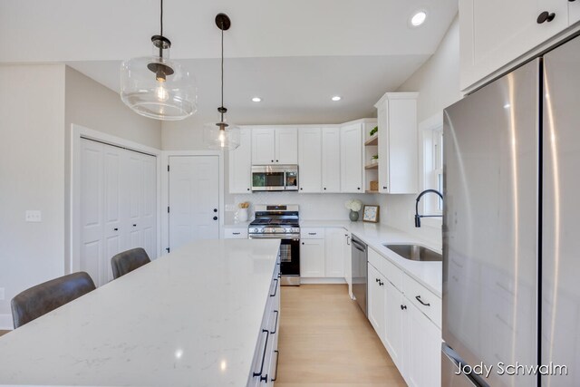 kitchen with light stone counters, stainless steel appliances, white cabinetry, and sink