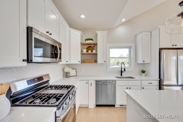 kitchen featuring stainless steel appliances, sink, pendant lighting, white cabinets, and light hardwood / wood-style floors