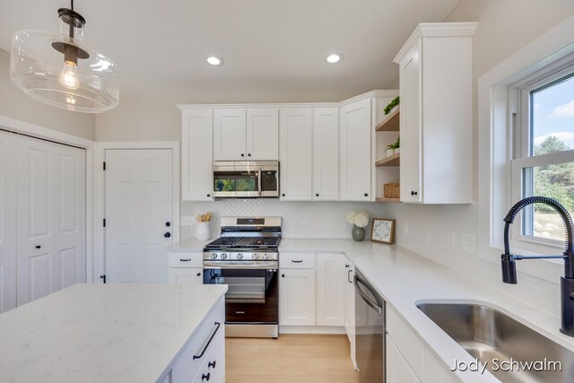 kitchen with appliances with stainless steel finishes, sink, pendant lighting, light hardwood / wood-style flooring, and white cabinetry