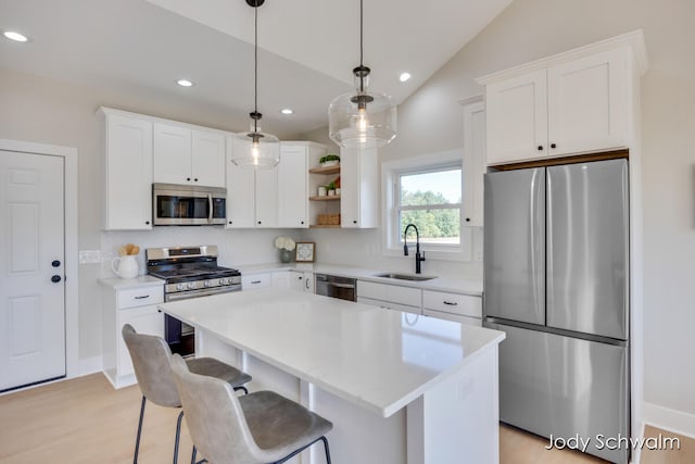 kitchen with sink, vaulted ceiling, appliances with stainless steel finishes, decorative light fixtures, and a kitchen island