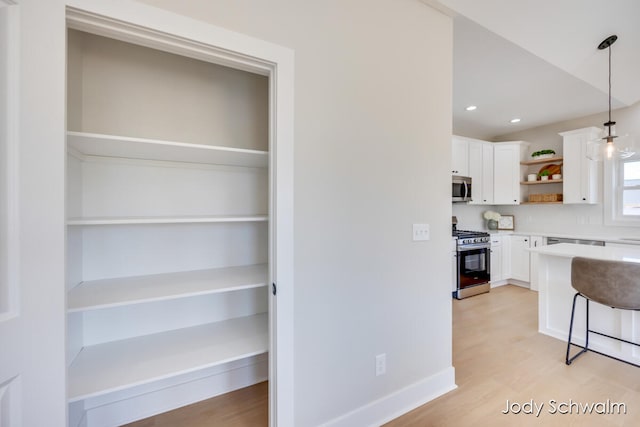 kitchen with white cabinets, light hardwood / wood-style floors, decorative light fixtures, and appliances with stainless steel finishes