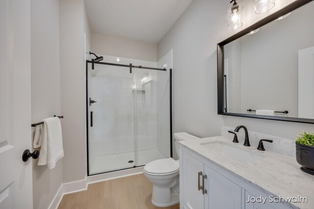 bathroom with wood-type flooring, vanity, toilet, and a shower with door