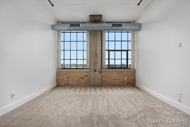 spare room with a textured ceiling, carpet floors, and brick wall