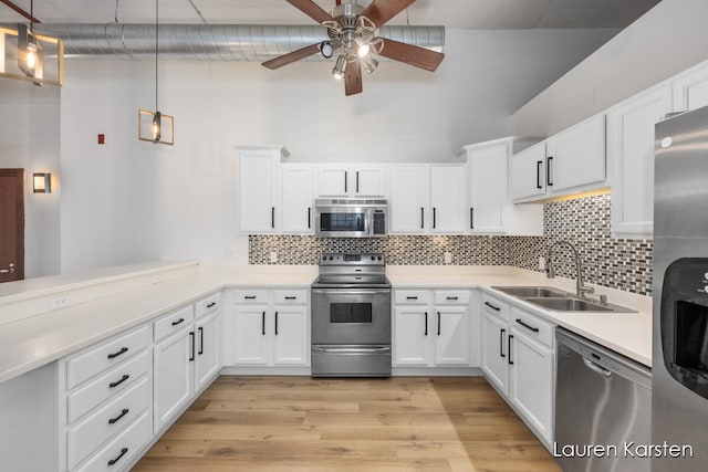 kitchen featuring white cabinets, decorative light fixtures, appliances with stainless steel finishes, and light hardwood / wood-style flooring