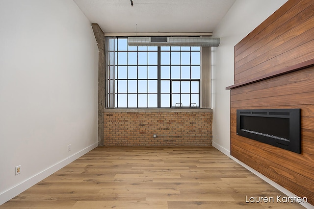 unfurnished living room with brick wall and light hardwood / wood-style floors