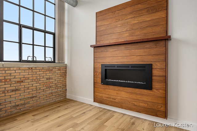 unfurnished living room featuring brick wall and light hardwood / wood-style floors