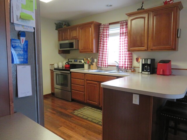 kitchen with kitchen peninsula, appliances with stainless steel finishes, dark hardwood / wood-style flooring, a kitchen breakfast bar, and sink