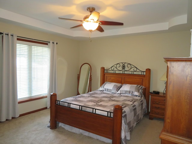 carpeted bedroom with ceiling fan and a raised ceiling